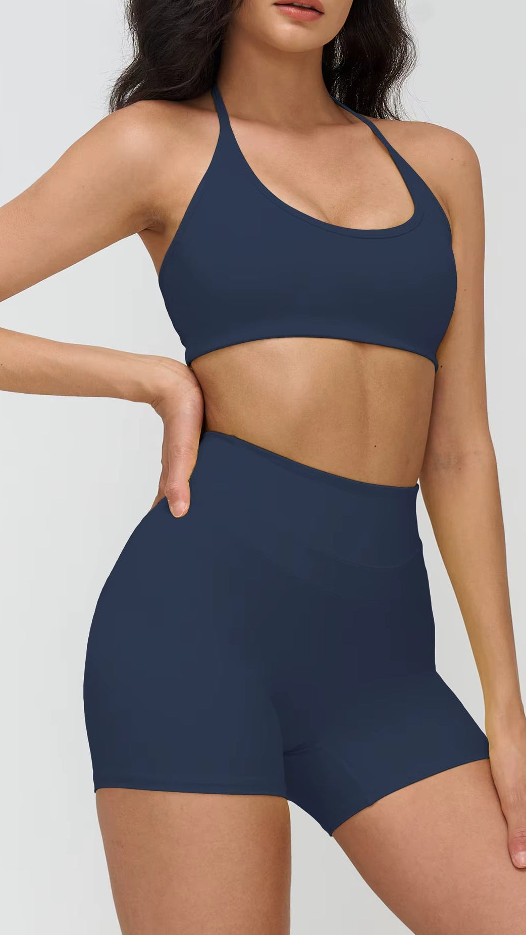 Woman wearing a navy blue sports bra and shorts on a light gray background